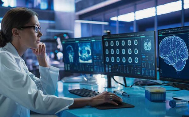 A scientist inspects brain scans at a desk monitor.