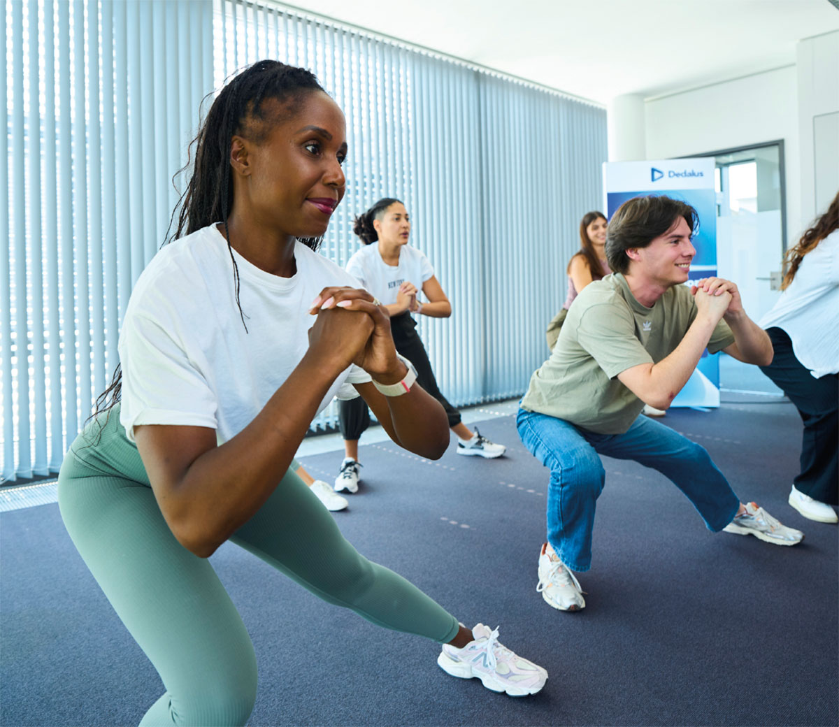 Menschen bewegen: Interview mit Stefanie Heinen, Dedalus HealthCare. Dienstagmittag, 12:30 Uhr. In Raum C2.2 des Bonner Headquarters treffen sich fünf Mitarbeiterinnen und Mitarbeiter, einige im Sportoutfit, andere in normaler Kleidung. 30 weitere haben sich aus dem Homeoffice online dazugeschaltet. Die „Bewegte Pause“ steht an, ein Angebot des Betrieblichen Gesundheitsmanagements, um den Mitarbeiterinnen und Mitarbeitern mit Dehnen, Stretchen, Mobilisations- und leichten Kraftübungen eine halbstündige Auszeit von der Arbeit zu ermöglichen.