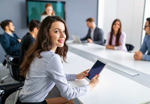Mujer sonriendo y sujetando tablet en una reunión de trabajo