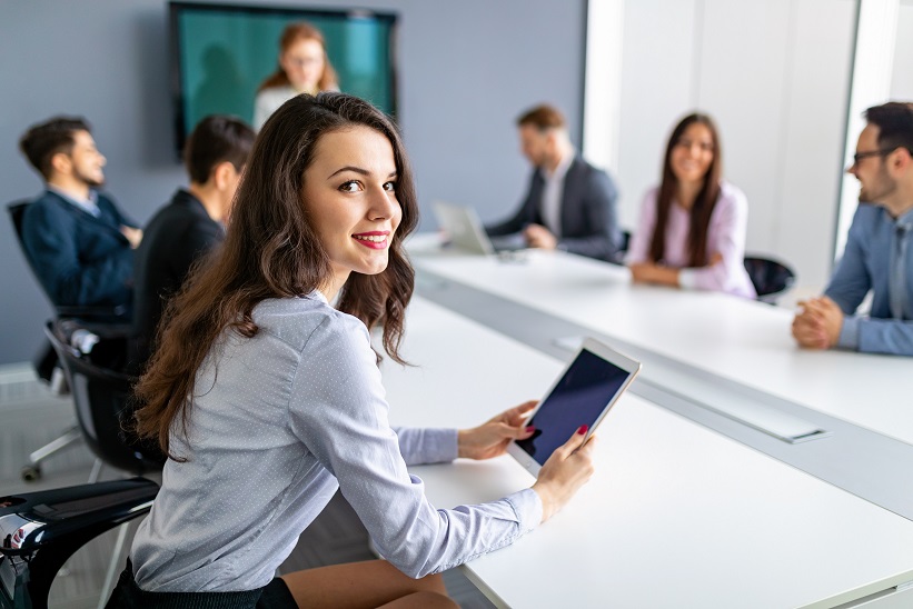 Mujer sonriendo y sujetando una tablet en una reunión de trabajo