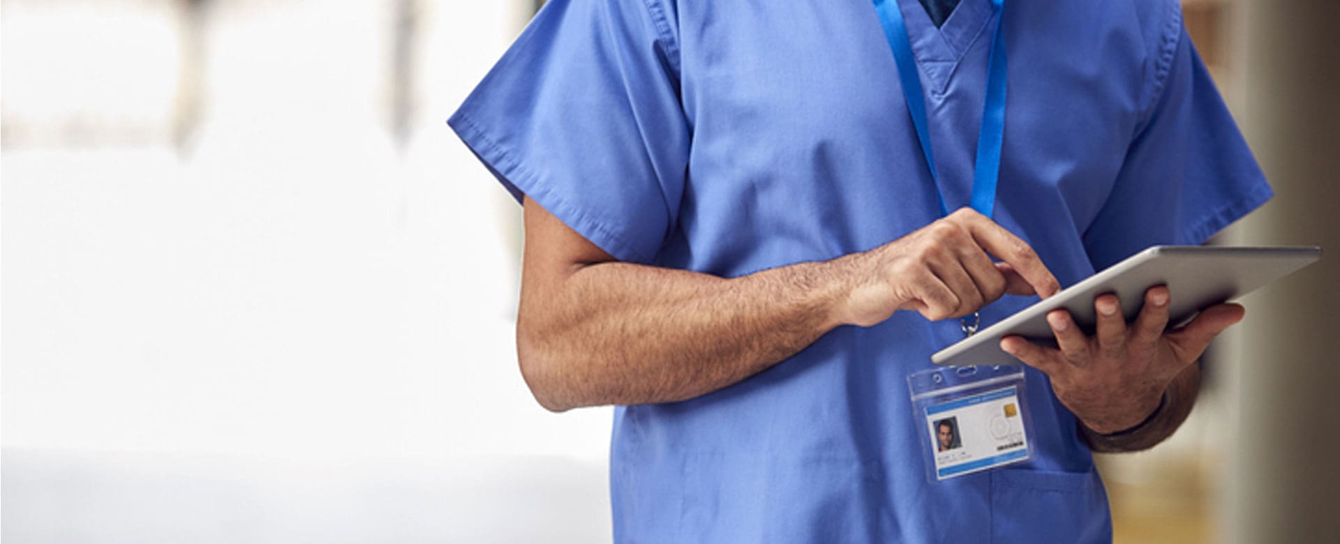 close up of male doctor wearing short sleeved blue gown using an ipad in his hands